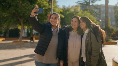Mother and daugthers making selfie by the smartphone standing together at park