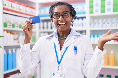 Eczanede çalışan Afrikalı kadın elinde kredi kartıyla başarıyı mutlu bir gülümsemeyle ve kazanan ifadeyle kutluyor. 