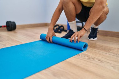 Genç Arap adam spor merkezinde yoga minderi kıvırıyor.