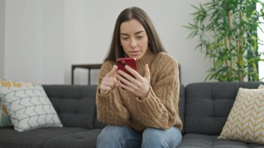 Evdeki kanepede oturan akıllı telefon kullanan genç, güzel İspanyol kadın.