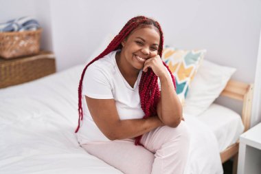 Afro-Amerikalı kadın yatakta kendinden emin bir şekilde gülümsüyor.