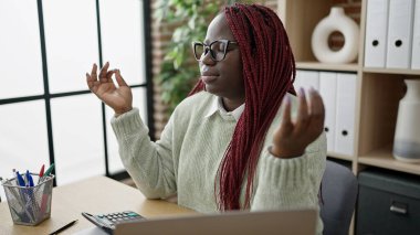 Saçları örgülü bir iş adamı olan Afrikalı kadın ofiste yoga egzersizi yapıyor.