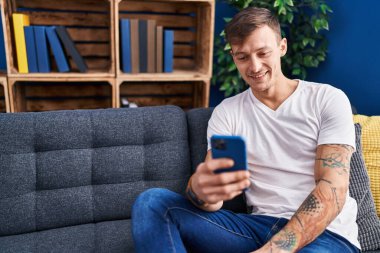 Genç adam evde koltukta oturan smartphone kullanarak