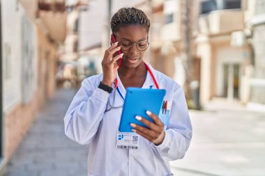 Afro-Amerikalı kadın doktor akıllı telefondan konuşuyor. Sokakta dokunmatik ped kullanıyor.