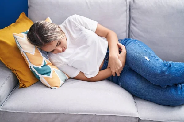 Young Blonde Woman Suffering Menstrual Pain Lying Sofa Home —  Fotos de Stock