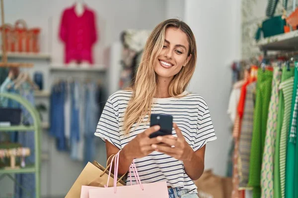 在服装店使用智能手机时 年轻的金发女顾客带着自信的笑容 — 图库照片