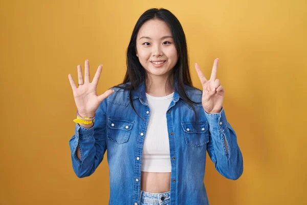 Молодая Азиатка Стоящая Желтом Фоне Показывающая Пальцами Номер Семь Улыбаясь — стоковое фото