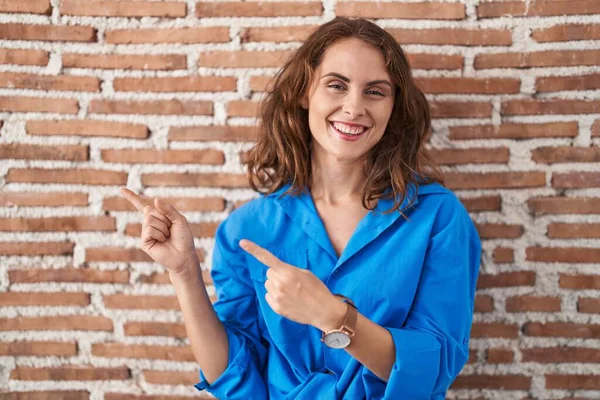 美しいブルネット女性立ち上がっレンガの壁笑顔と見てカメラポインティングで二つの手と指で側面 — ストック写真