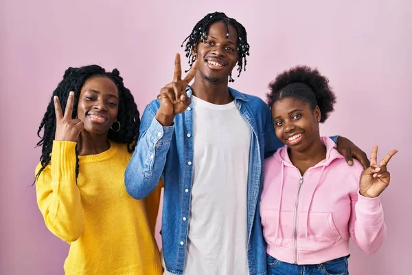 一组三个年轻的黑人站在粉红的背景上 高兴地微笑着 用手指在镜头前眨眼示意胜利 第二点 — 图库照片
