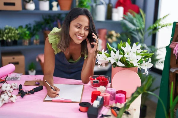 Young Hispanic Woman Florist Talking Smartphone Writing Document Florist Store — Stockfoto