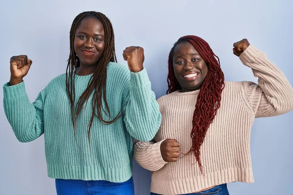Dwie Afrykańskie Kobiety Stojące Nad Niebieskim Tłem Pokazujące Mięśnie Ramion — Zdjęcie stockowe