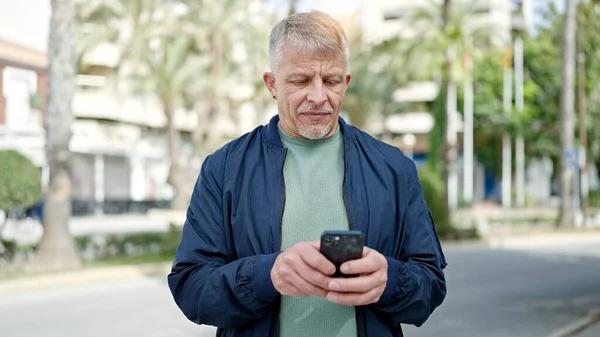 中年白发男子在公园里用带有严肃表情的智能手机 — 图库照片