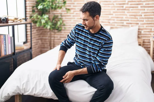 Young Hispanic Man Suffering Knee Injury Sitting Bed Bedroom — Φωτογραφία Αρχείου
