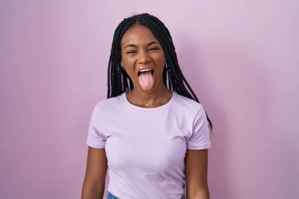 Африканская Американка Косичками Стоящая Розовом Фоне Торчащая Языком Довольная Смешным — стоковое фото