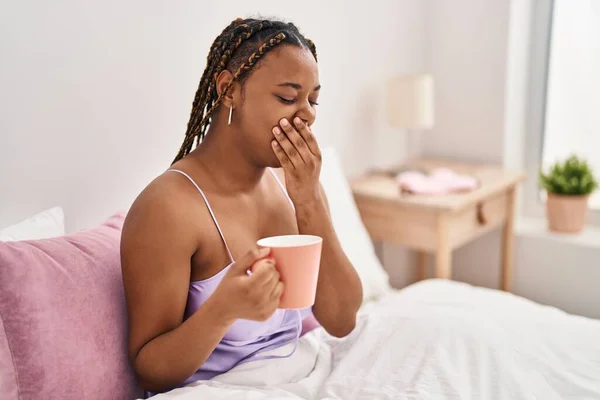 非洲裔美国妇女坐在床上打呵欠 在卧室喝咖啡 — 图库照片