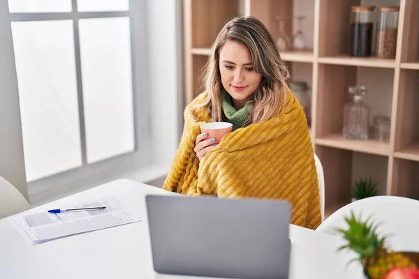 stock image Young woman covering with blanket drinking coffe using laptop at home