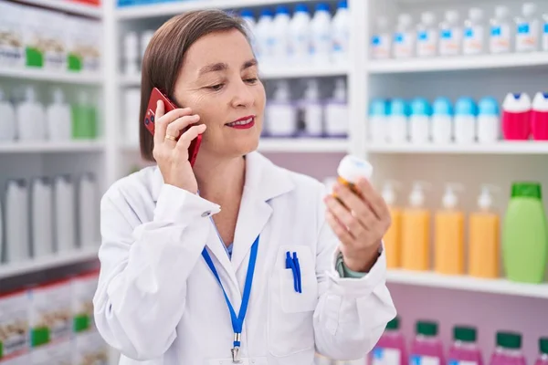 Middle Age Woman Pharmacist Holding Pills Bottle Talking Smartphone Pharmacy — Fotografia de Stock