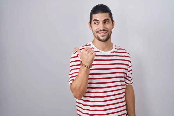 一个有着长发的西班牙男人站在孤立的背景上 面带微笑 面带微笑 并以大拇指指向旁边 — 图库照片