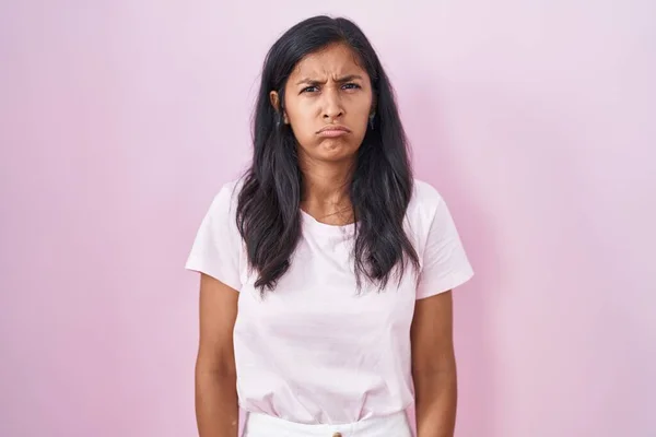 Young hispanic woman standing over pink background skeptic and nervous, frowning upset because of problem. negative person.