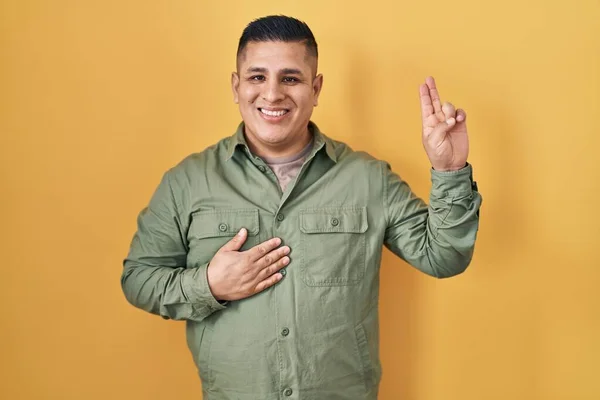 Jovem Hispânico Sobre Fundo Amarelo Sorrindo Jurando Com Mão Peito — Fotografia de Stock