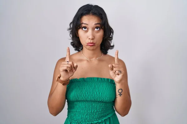 stock image Young hispanic woman standing over isolated background pointing up looking sad and upset, indicating direction with fingers, unhappy and depressed. 