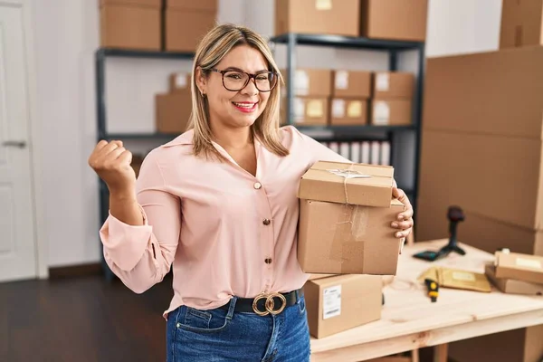 stock image Young hispanic woman working at small business ecommerce screaming proud, celebrating victory and success very excited with raised arm 