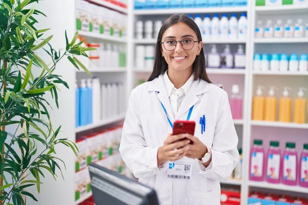 年轻美丽的惊慌失措的女药剂师用智能手机在药店工作 — 图库照片