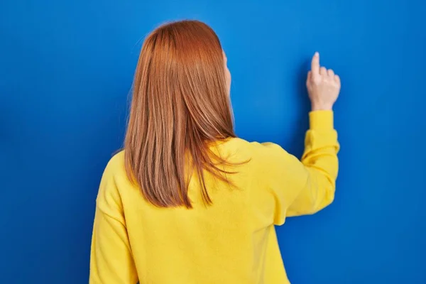 年轻女子站在蓝色的背景上 手指头倒立在前方 — 图库照片
