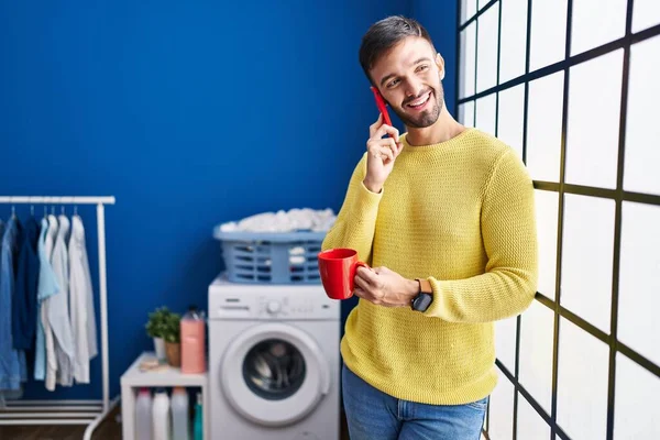 Young Hispanic Man Talking Smartphone Drinking Coffee Waiting Washing Machine — Stock Photo, Image