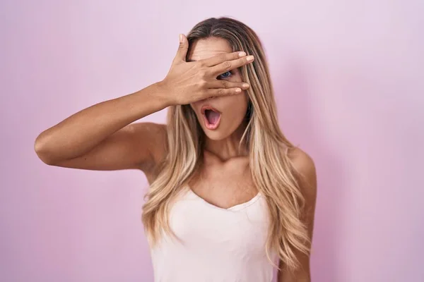 Young Blonde Woman Standing Pink Background Peeking Shock Covering Face — Stock Fotó