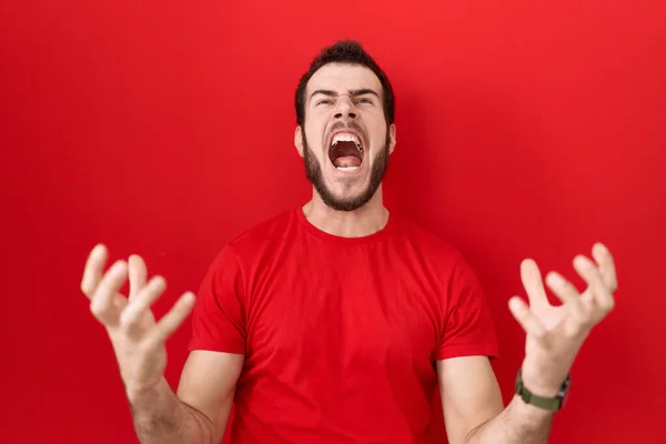 カジュアルな赤いTシャツを着た若いヒスパニック系の男が狂った叫び 積極的な表現と腕を上げて叫びました フラストレーションコンセプト — ストック写真
