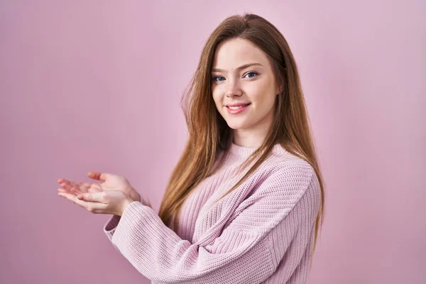 年轻的高加索女人站在粉色的背景上 双手张开手掌 展示复制的空间 露出兴奋的笑容 — 图库照片
