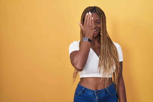 Африканская Американка Плетеными Волосами Стоящая Жёлтом Фоне Закрывая Один Глаз — стоковое фото