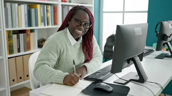 大学図書館のノートにコンピュータライティングを使用して編組髪の学生を持つアフリカの女性 — ストック写真