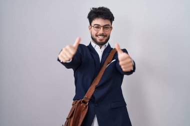 Sakallı, iş kıyafetleri giyen, elinde olumlu bir jest yapan, gülümseyen ve başarı için sevinen İspanyol bir adam. kazanan jest. 