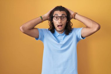 Sarı arka planda dikilen İspanyol genç adam deli ve elleri başının üstünde korkmuş, korkmuş ve ağzı açık şoktan şaşırmış. 