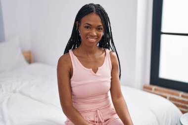Afro-Amerikalı kadın yatakta kendinden emin bir şekilde gülümsüyor.