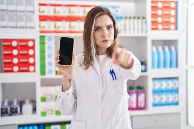 Eczanede çalışan sarışın, beyaz bir kadın akıllı telefon ekranını kamerayı işaret ediyor ve sen kendine güvenen ciddi bir hareket yapıyorsun. 