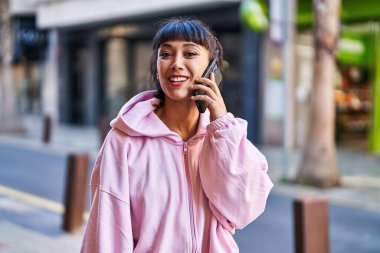 Gülümseyen genç bir kadın caddedeki akıllı telefondan konuşuyor.