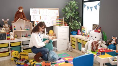 Young caucasian woman working as teacher tidying up at kindergarten