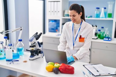 Laboratuvarda çalışan genç ve güzel İspanyol bilim kadını laptopu kullanıyor.