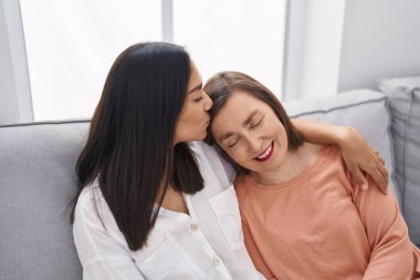 Two women mother and daughter sitting on sofa together at home