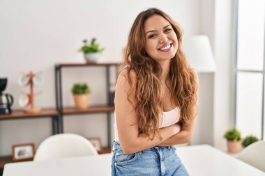 Young beautiful hispanic woman smiling confident standing with arms crossed gesture at home