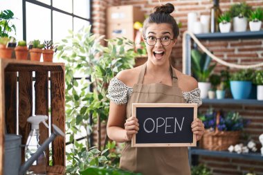 Hispanic woman working at florist holding open sign celebrating crazy and amazed for success with open eyes screaming excited. 