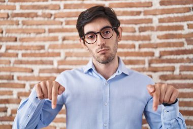 Tuğla duvar arkasında dikilen genç İspanyol adam üzgün ve üzgün görünüyor, parmaklarıyla yönü gösteriyor, mutsuz ve depresif.. 