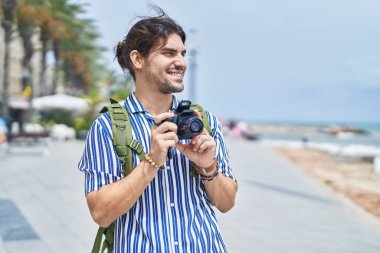 Genç İspanyol turist sırt çantası takıyor. Sahilde profesyonel kamera kullanıyor.