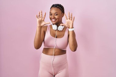 Spor kıyafetleri ve kulaklıkları takan Afrikalı Amerikalı bir kadın 10 numarayı gösterip gösterirken kendinden emin ve mutlu gülümsüyor.. 