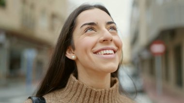 Young beautiful hispanic woman smiling confident looking to the sky at street