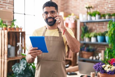 Genç Arap çiçekçi çiçekçide dokunmatik ped kullanarak akıllı telefondan konuşuyor.