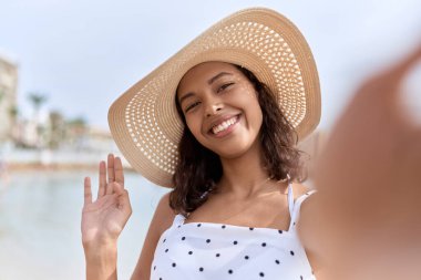 Yazlık şapkalı genç Afrikalı Amerikalı kadın deniz kenarında fotoğraf çekiyor.